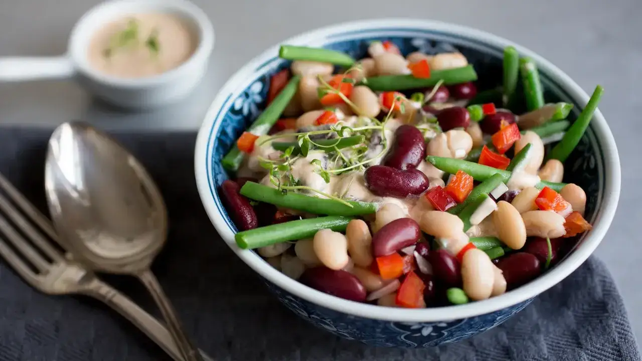 Ein bunter Bohnensalat mit gr&uuml;nen Bohnen, roten und wei&szlig;en Bohnen, Paprikaw&uuml;rfeln und einer cremigen So&szlig;e, garniert mit frischen Kr&auml;utern.