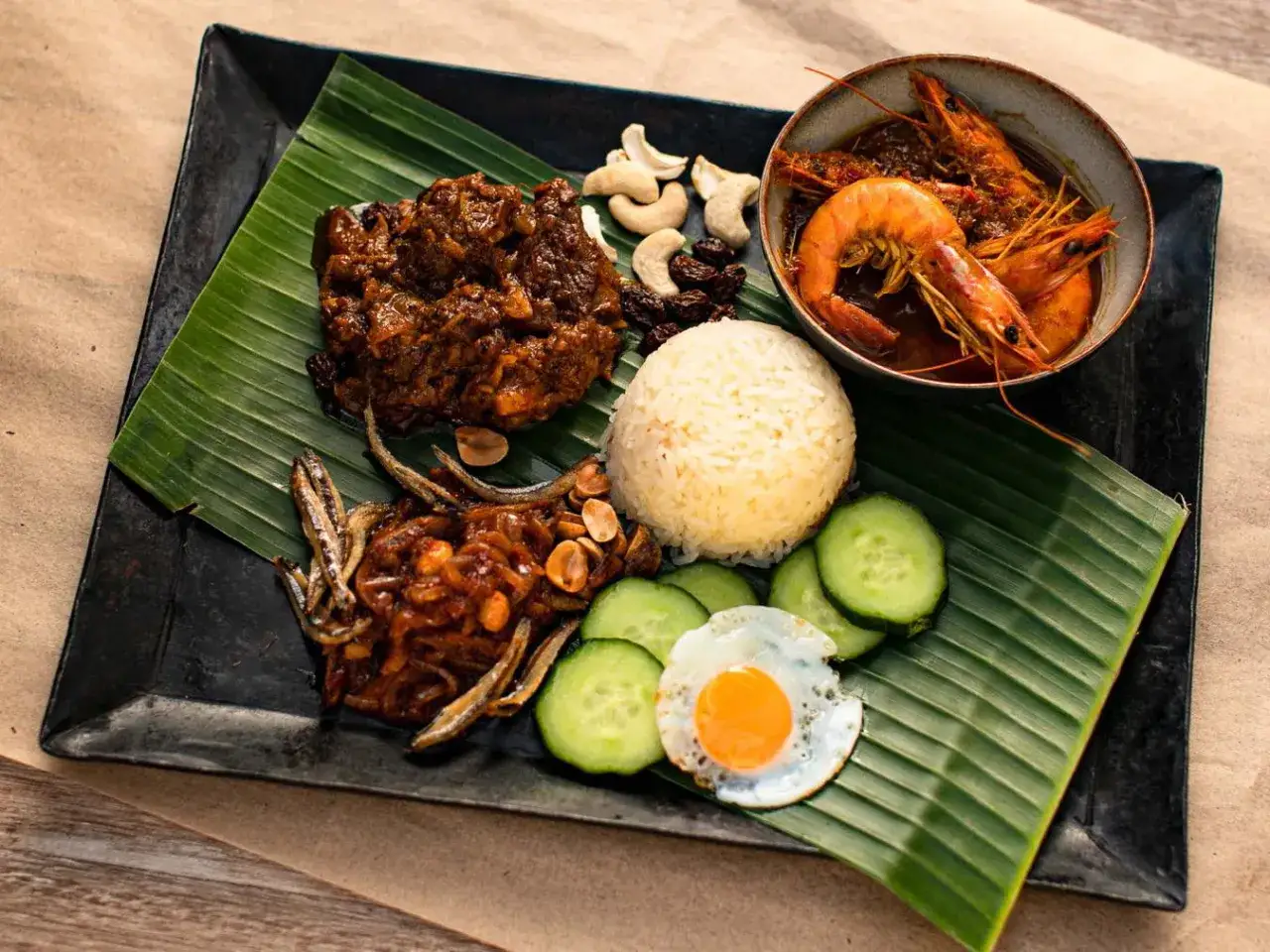 Nasi lemak: Reis, scharfe Garnelen, Sardellen, Spiegelei, Gurken, Cashewkerne und Rosinen auf Bananenblatt.
