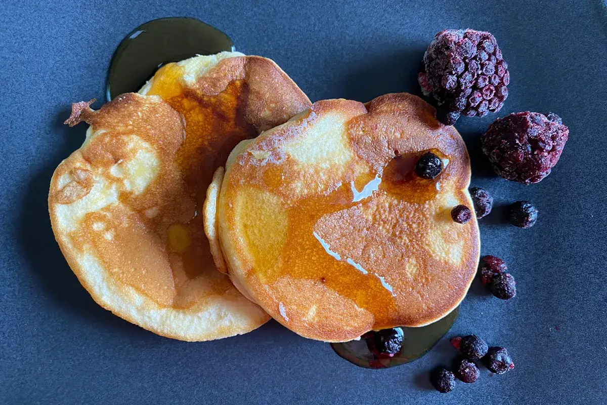 Zwei goldbraune Pancakes ohne Backpulver, beträufelt mit Sirup und garniert mit gefrorenen Beeren.