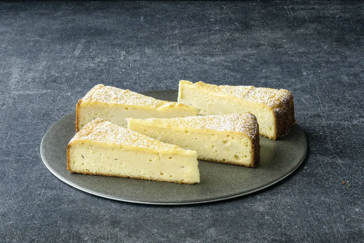 Saftige Scheiben eines Ricotta Mandel Kuchens, bestäubt mit Puderzucker, auf einem grauen Teller.