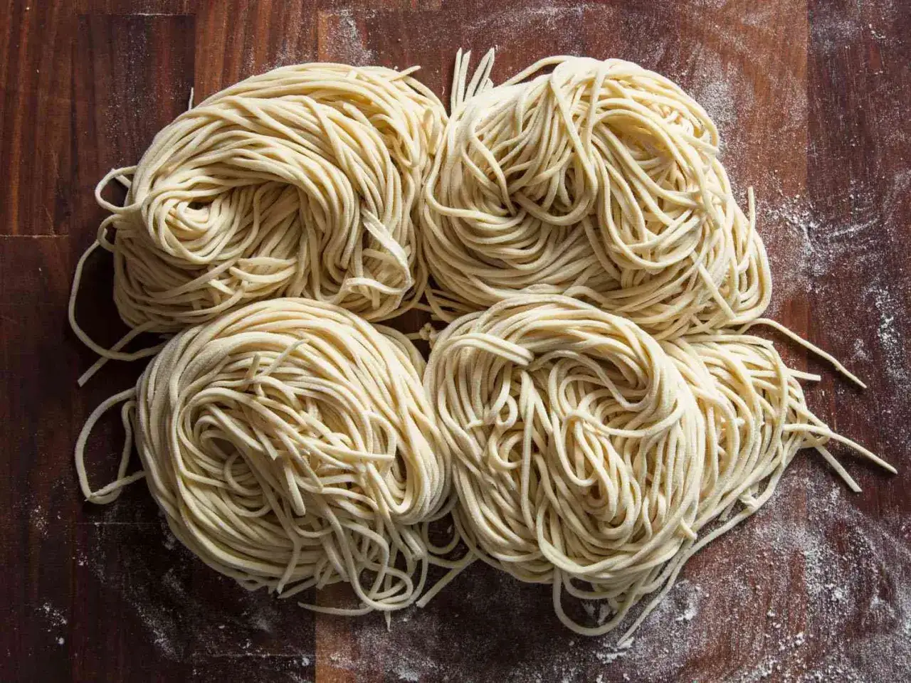 Vier Portionen frischer Ramen-Nudeln liegen auf einem Holztisch. Perfekt für dein nächstes Projekt, ramen selber machen!
