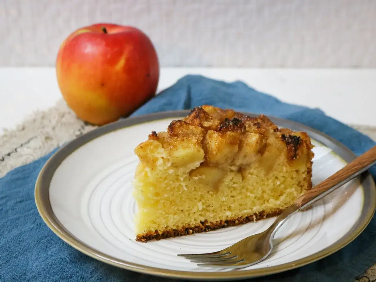Ein Stück von Omas weltbester Apfelkuchen, saftig und mit knuspriger Kruste, daneben ein frischer Apfel.