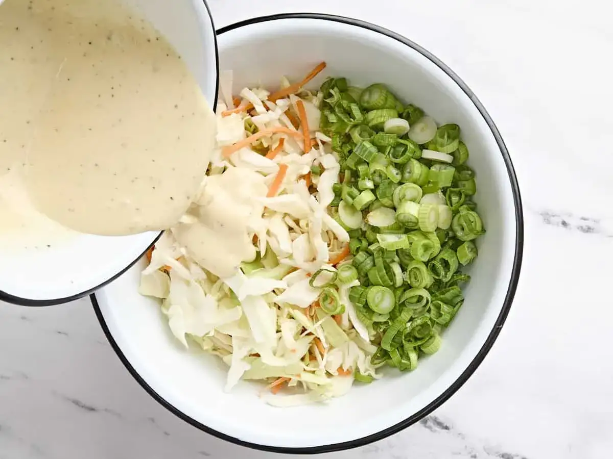 Für das Rezept Coleslaw Original wird cremiges Dressing über fein geschnittenen Kohl, Karotten und Frühlingszwiebeln gegossen.