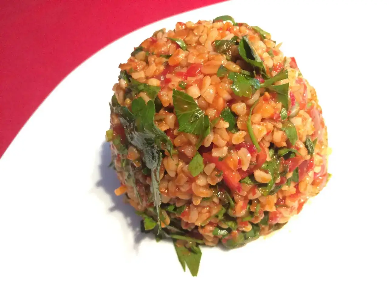Ein appetitlicher Bulgursalat, der aussieht wie das beste bulgursalat rezept, mit frischer Petersilie und Tomaten auf einem weißen Teller.