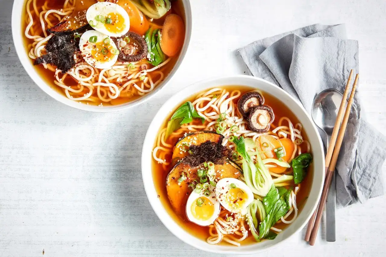 Zwei Schalen dampfender vegetarischer Ramen mit Nudeln, Ei, Pilzen, Kürbis und Gemüse.
