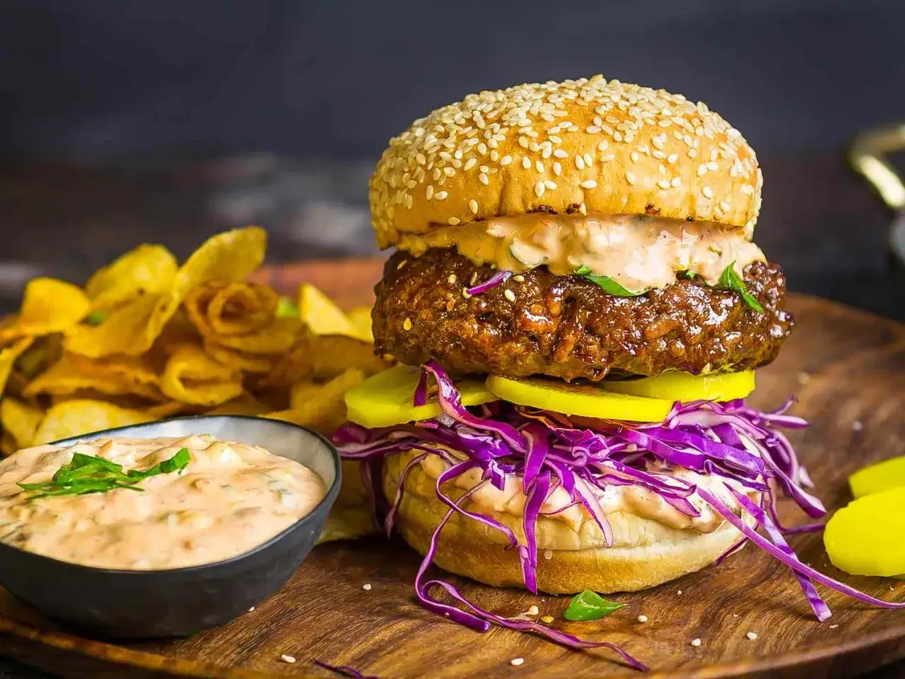 Saftiger korean burger mit Sesambrötchen, Rotkohl, Gurken und einer cremigen Sauce, serviert mit knusprigen Chips.