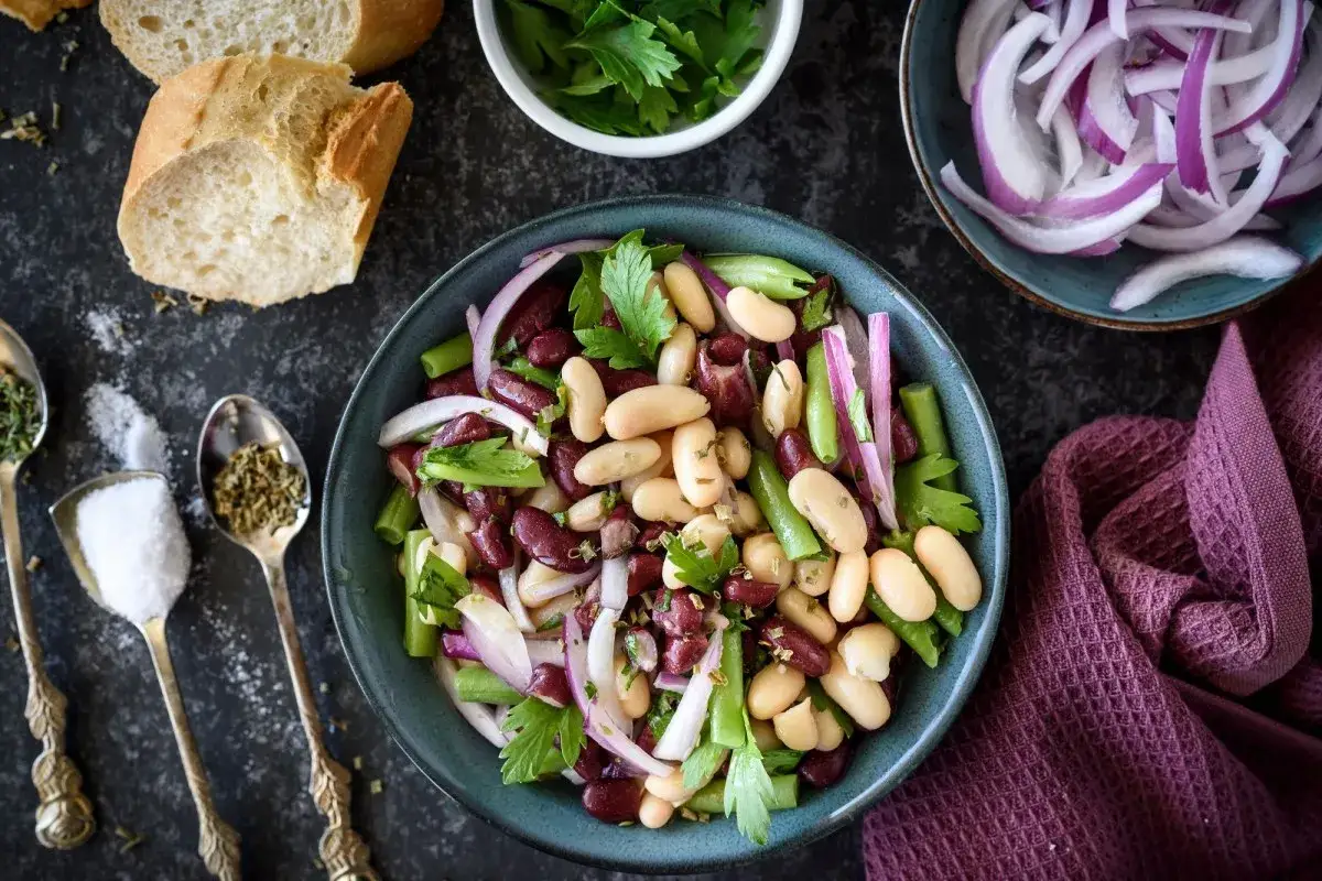 Bunter Bohnensalat mit roten Zwiebeln und Kräutern. Dazu passt frisches Baguette, das auf dem Bild zu sehen ist.