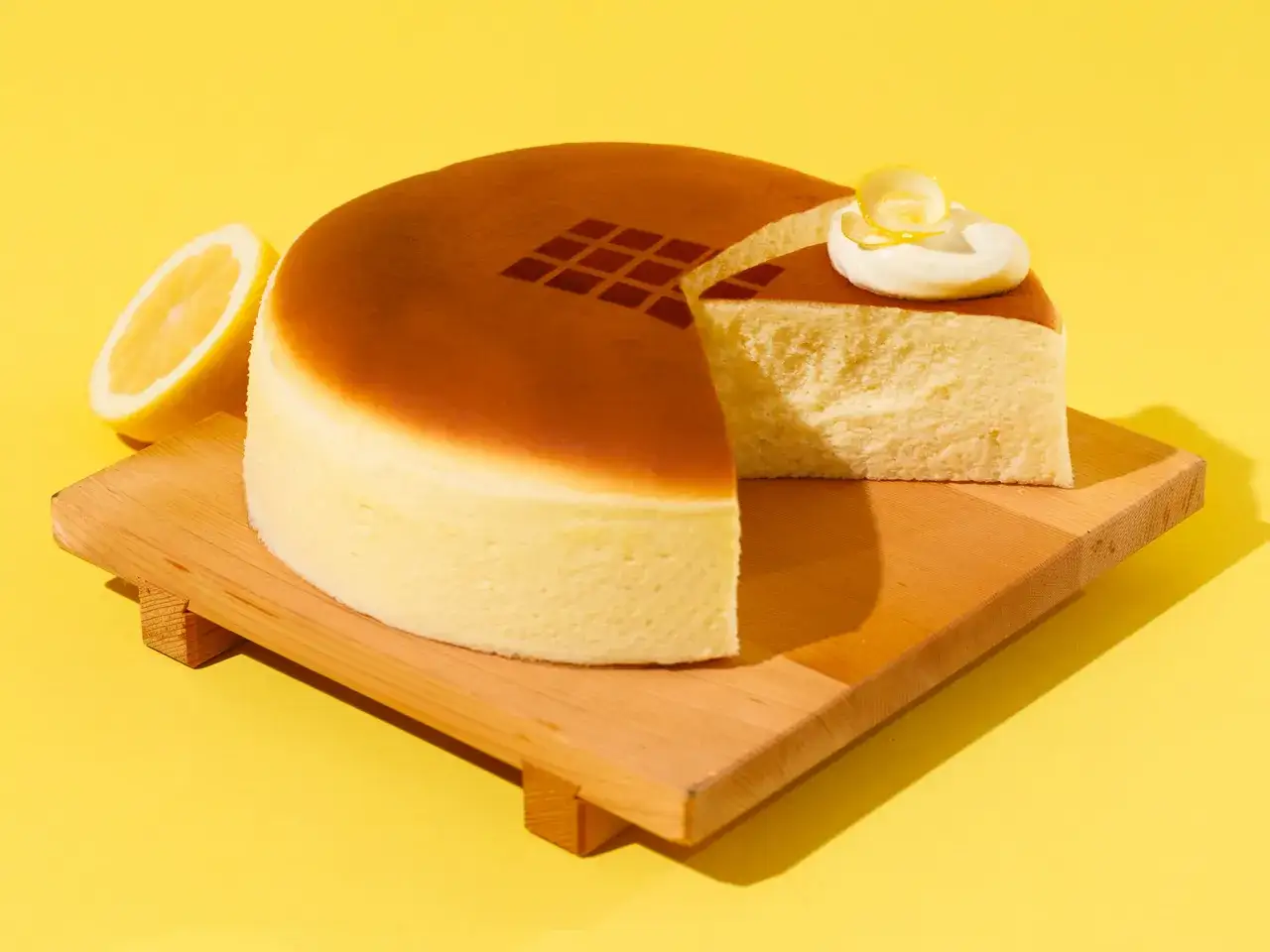 Ein luftiger japanischer Kuchen mit Zitronendekoration auf einem Holzbrett vor gelbem Hintergrund.