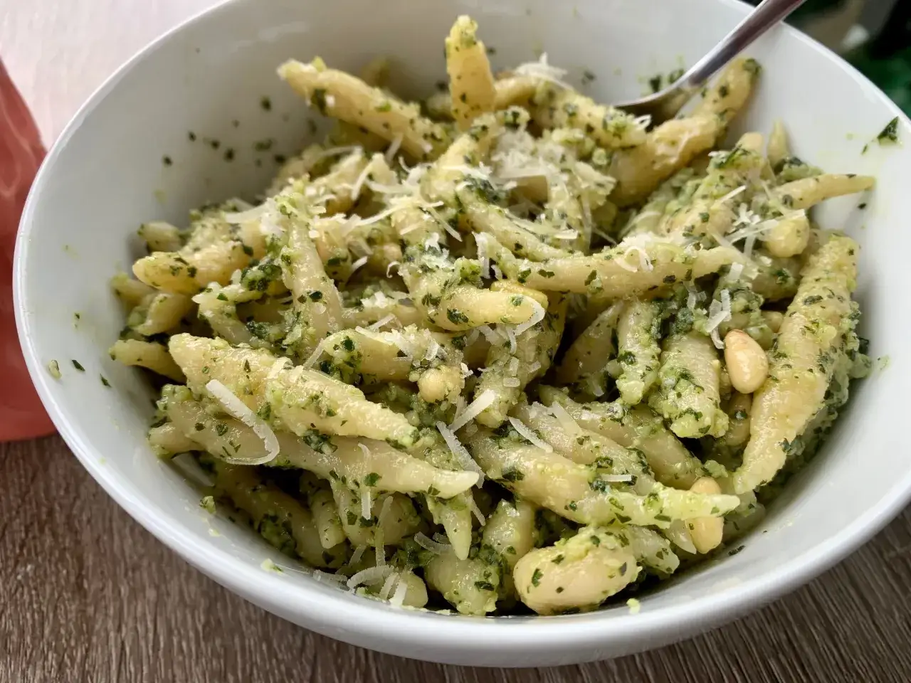 Eine Schüssel mit ligurischer Pasta, bedeckt mit leuchtend grünem Pesto, Pinienkernen und geriebenem Parmesan.