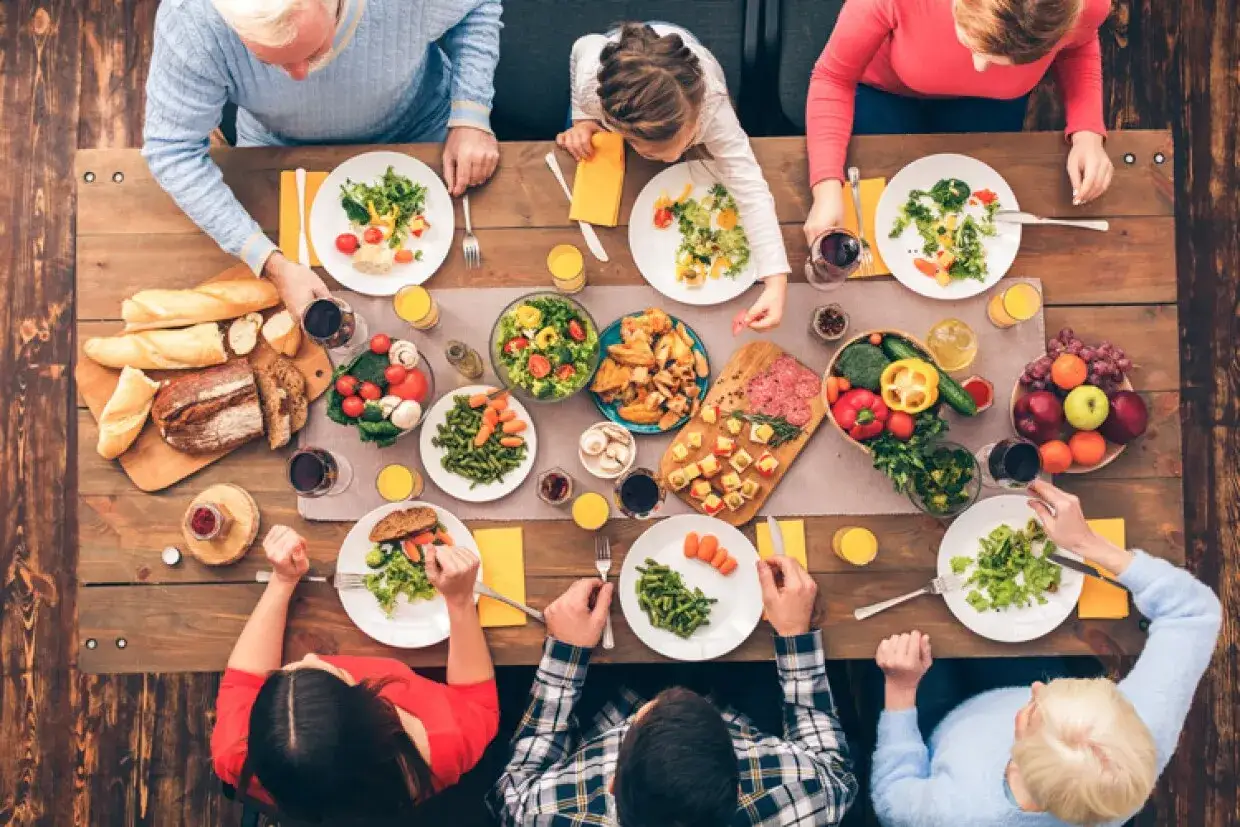 Familie genie&szlig;t ein &uuml;ppiges Abendessen mit Brot, Salat, Gem&uuml;se und Fleisch. So k&ouml;nnte aussehen, was essen Franzosen zum Abendessen.