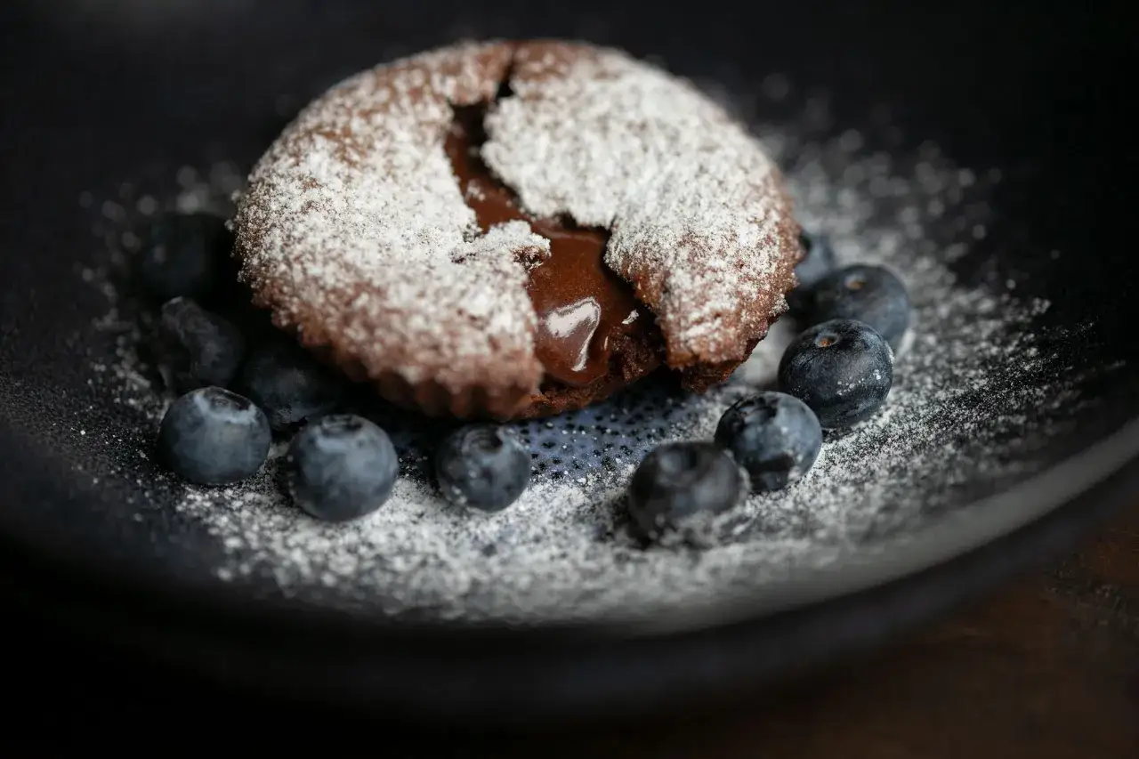 Ein warmer Moelleux au chocolat mit flüssigem Kern, bestäubt mit Puderzucker und garniert mit Blaubeeren.