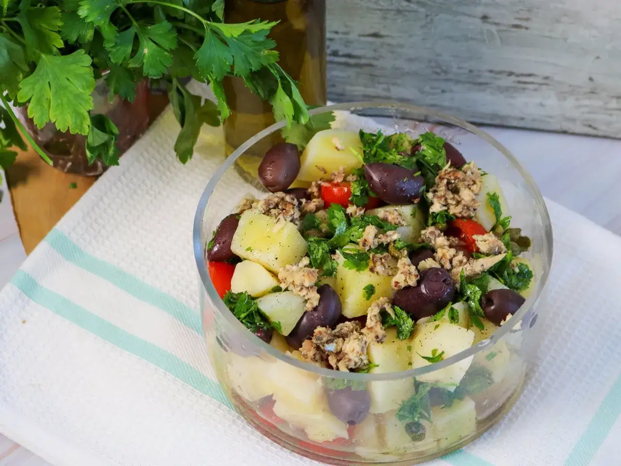 Frischer Kartoffelsalat mit Kapern, Oliven und Petersilie in einer Glasschüssel.
