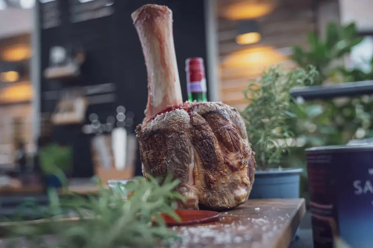Ein saftiges St&uuml;ck pulled beef mit Knochen, garniert mit Rosmarin, liegt auf einem Holzbrett.