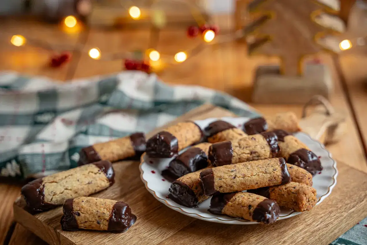 Leckere weihnachtskekse mit schokolade, die auf einem Holzbrett liegen. Im Hintergrund leuchten Lichterketten.