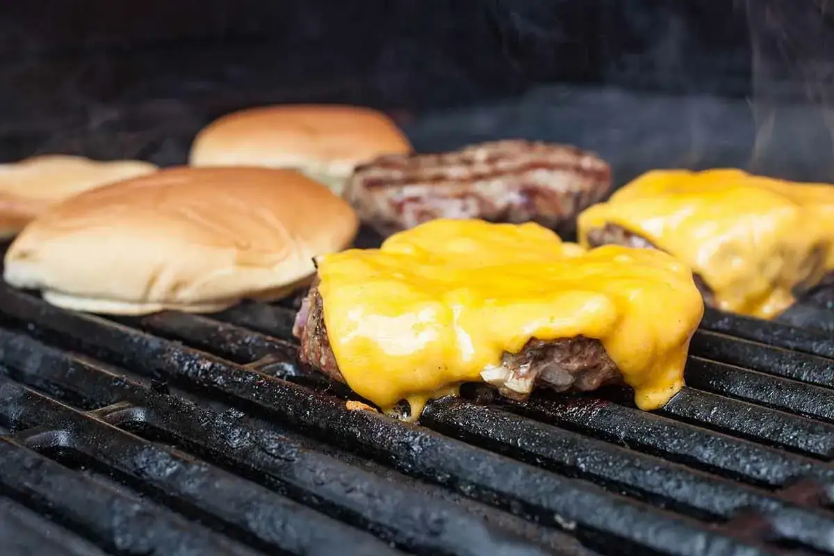 Burger zubereiten: saftige Patties mit geschmolzenem Käse auf dem Grill, daneben liegen die Brötchen.