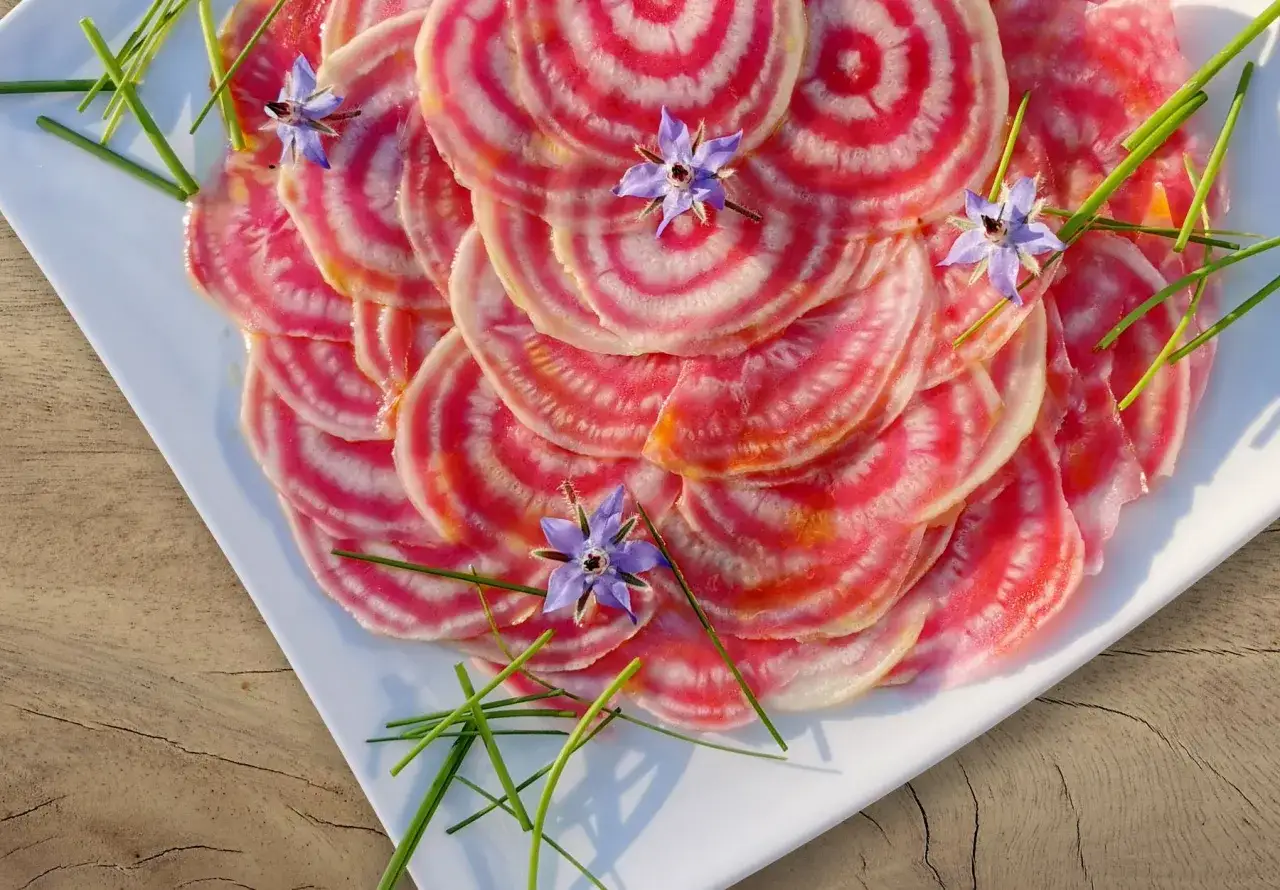 Bunte Ringelroten-Scheiben, garniert mit Borretschblüten und Schnittlauch. Ein optisch ansprechendes Gericht, das Lust auf ein Ringelbete Rezept macht.