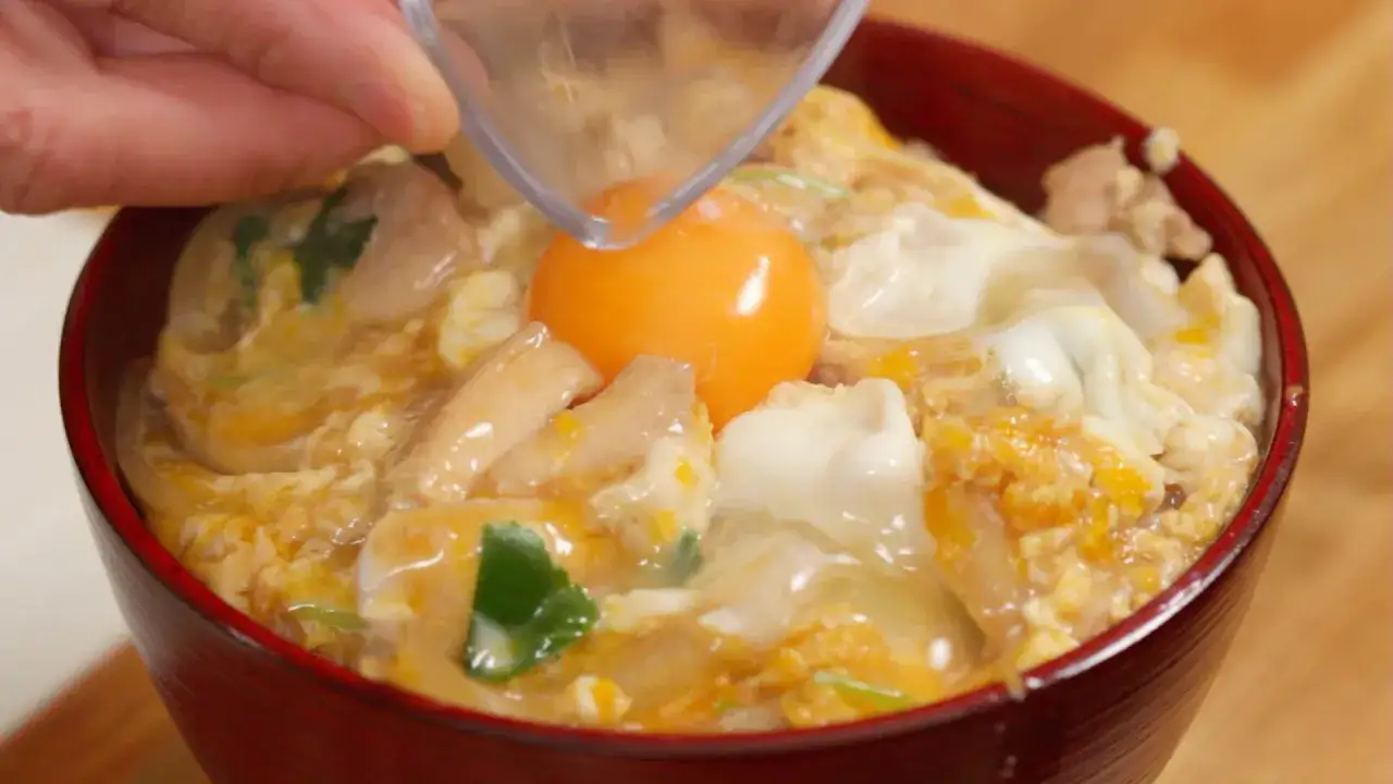 Ein rotes Schälchen mit einem köstlichen Oyakodon Rezept. Ein rohes Ei wird über Hühnchen und Reis gegeben.