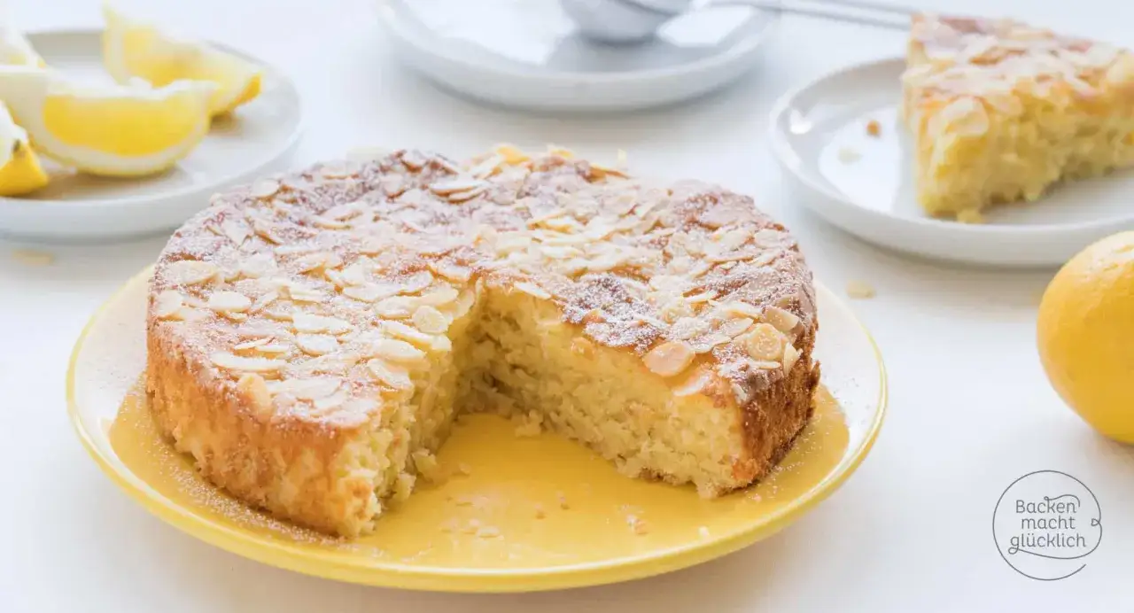 Ein saftiger Zitronenkuchen mit Mandelblättchen, perfekt für ein schnelles Financier Rezept. Mit Puderzucker bestäubt und Zitronenspalten garniert.