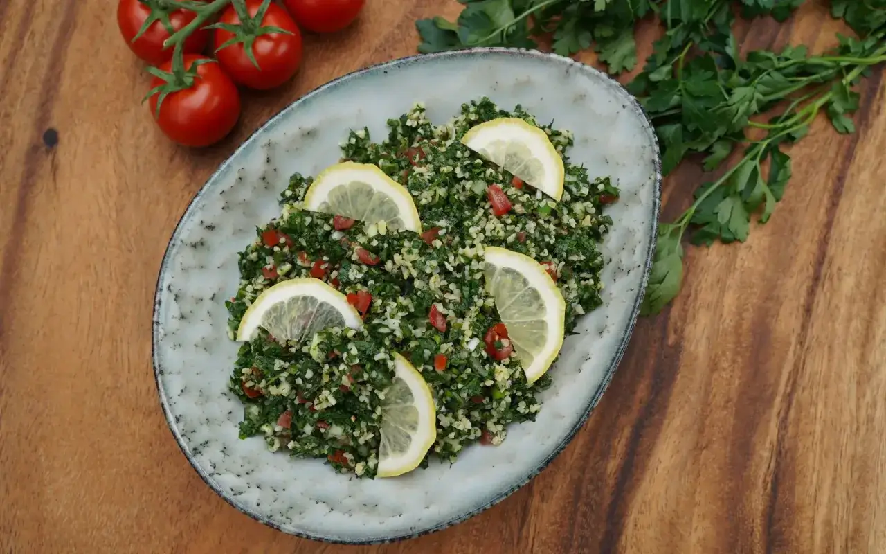 Frischer Tabouleh Salat, das Original-Rezept. Mit viel Petersilie, Tomaten, Bulgur und Zitronenspalten garniert.