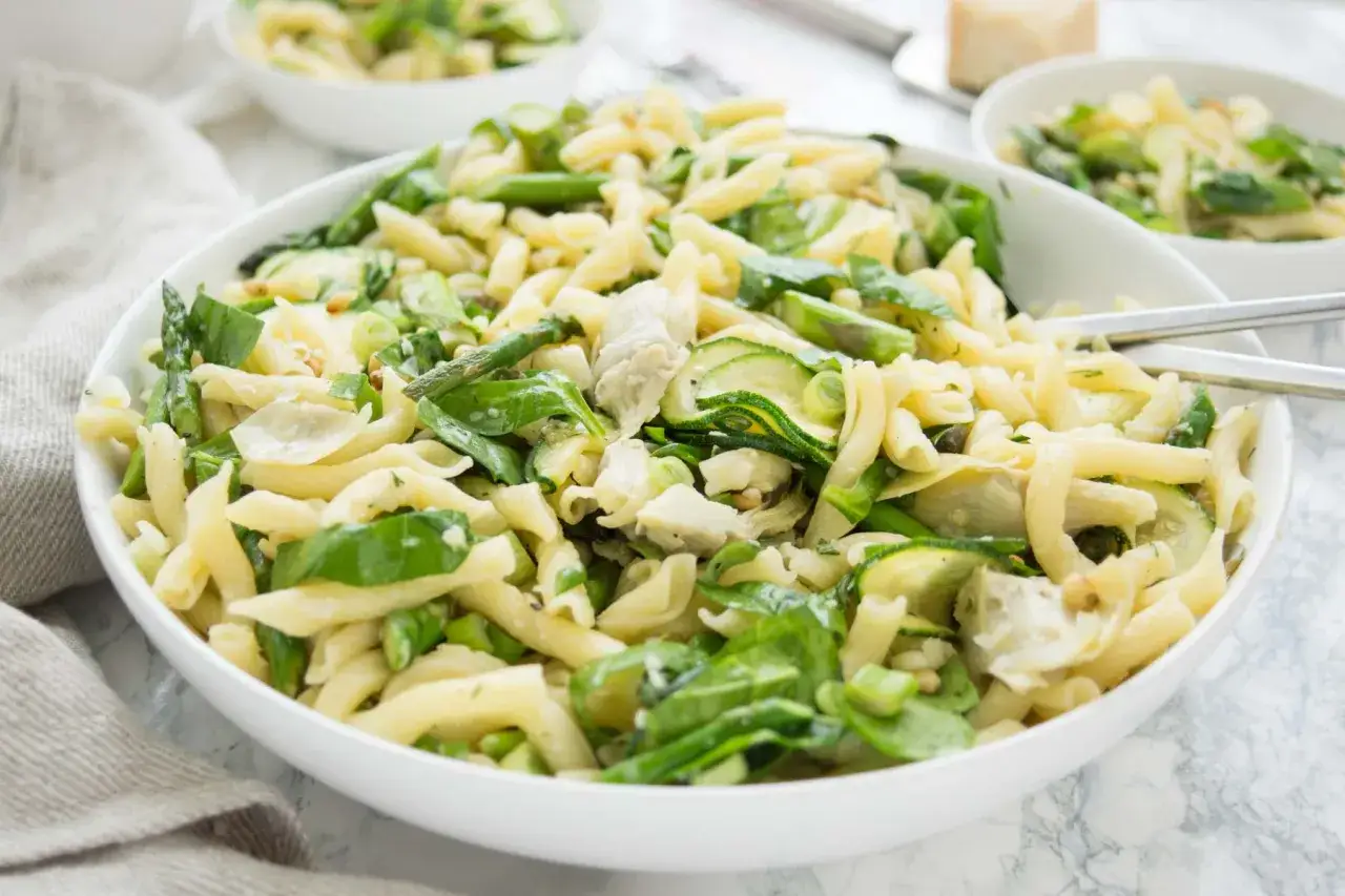 Ein köstlicher nudelsalat mit spargel, zucchini und grünen Blättern, serviert in einer weißen Schüssel.
