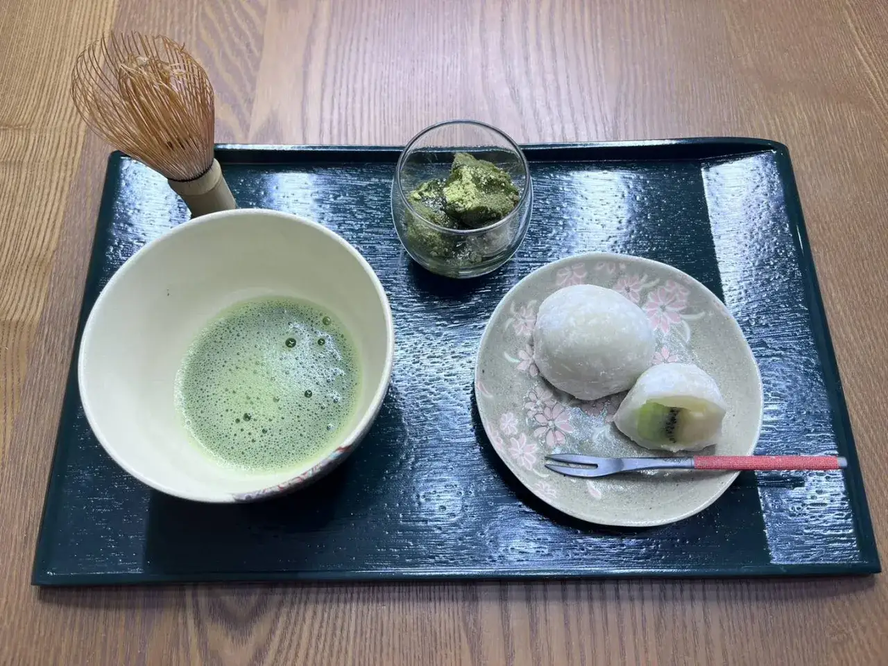Genussvolle japanische Desserts: Matcha-Schale, Daifuku mit Kiwi und ein Chasen auf einem Tablett.
