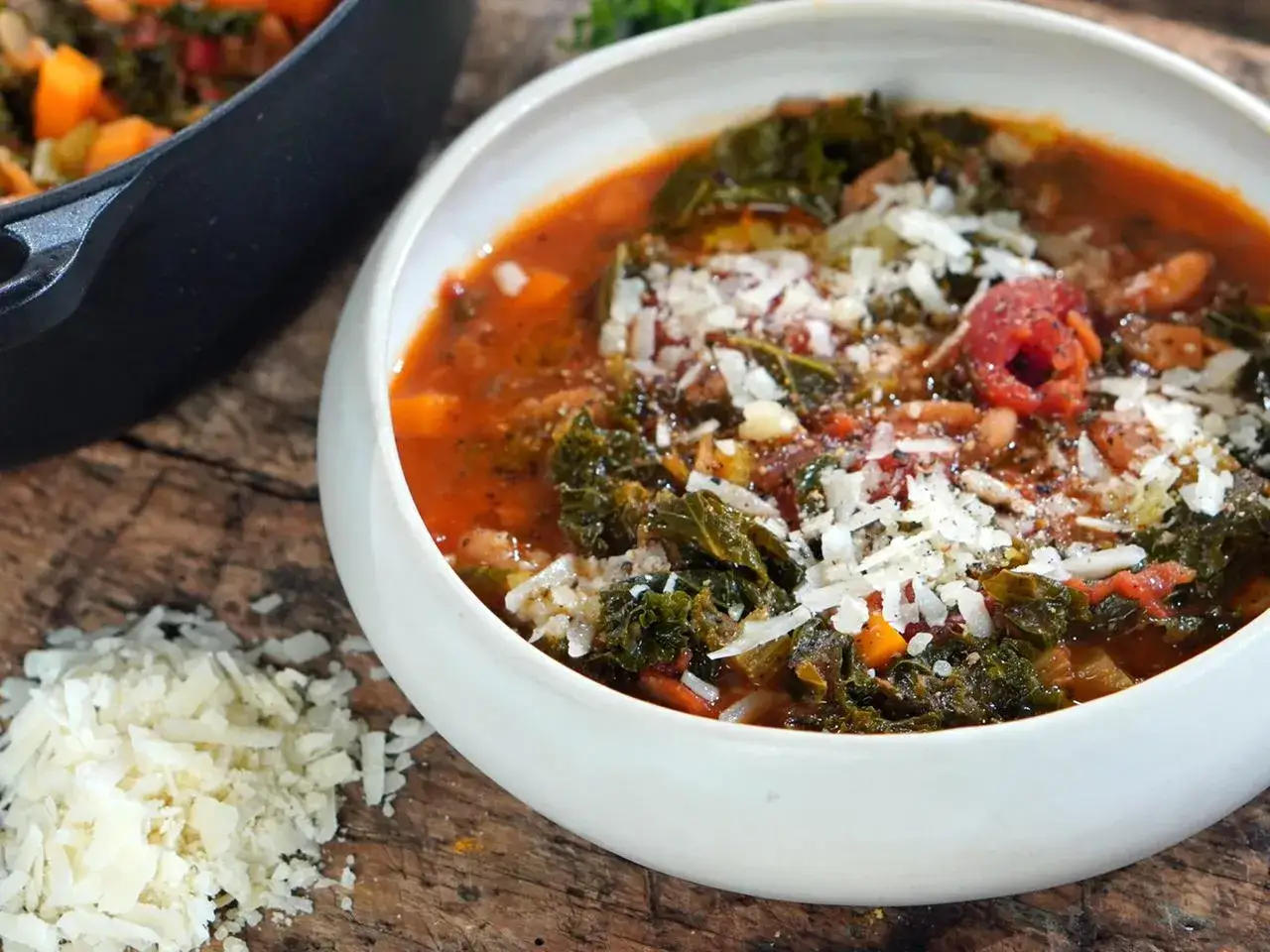 Herzhafte toskanische Bohnensuppe mit Grünkohl und geriebenem Parmesan, serviert in einer weißen Schüssel auf rustikalem Holz.