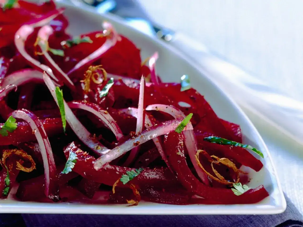 Ein Teller mit traditionellem Rote Bete Salat, garniert mit roten Zwiebeln und Petersilie.