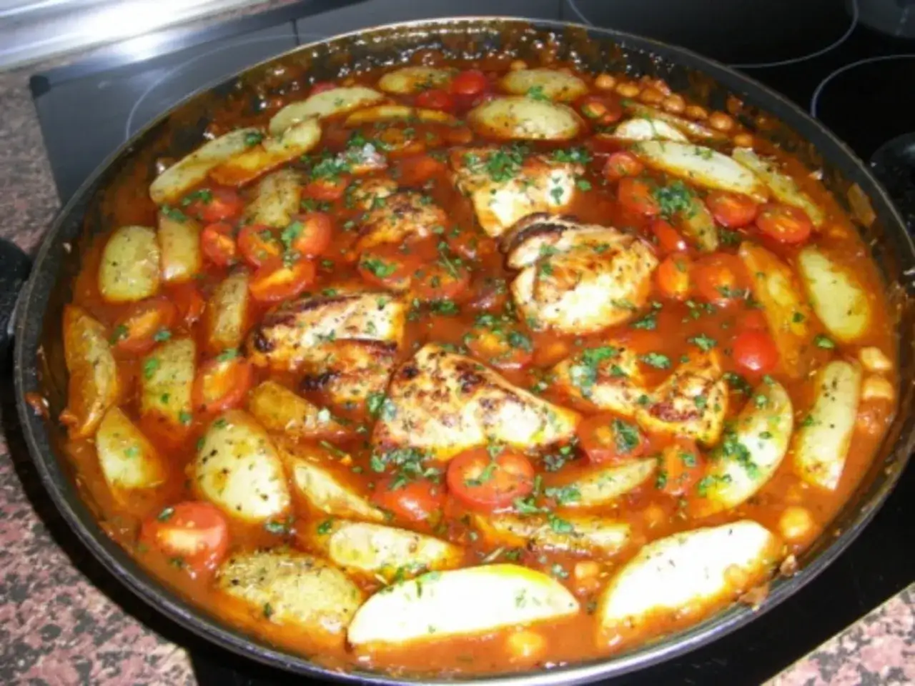 Herzhafter spanischer Eintopf mit Hähnchen, Kartoffelspalten, Kirschtomaten und Kichererbsen in einer würzigen Tomatensauce, garniert mit Petersilie.