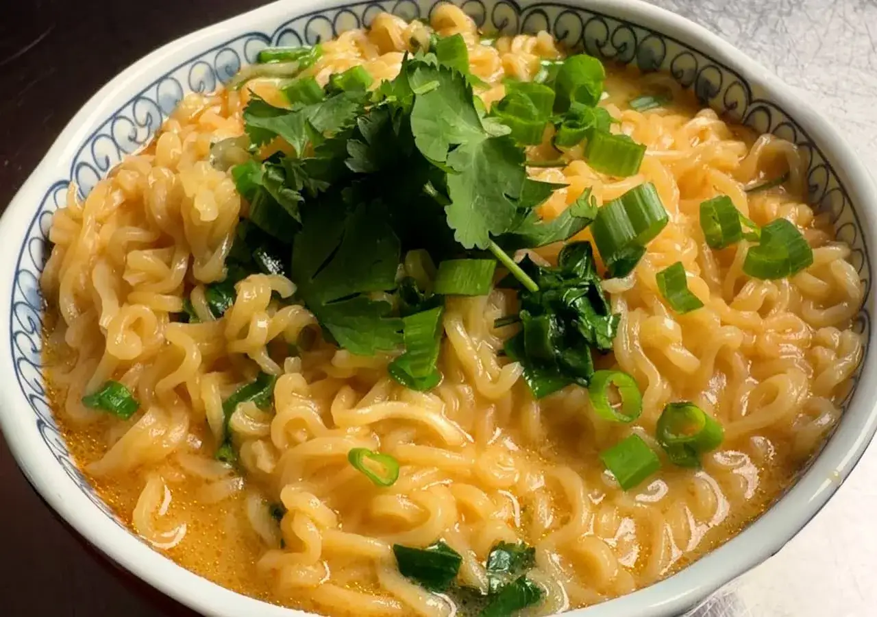 Eine Schüssel mit cremiger Laksa Suppe, garniert mit frischem Koriander und Frühlingszwiebeln.