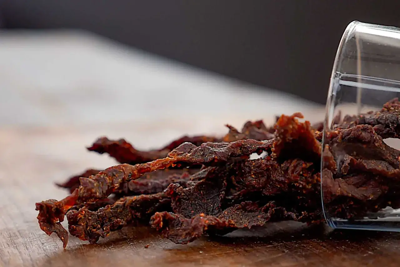 Ein Glas mit getrocknetem Rindfleisch, auch bekannt als Beef Jerky, liegt auf einem Holztisch.