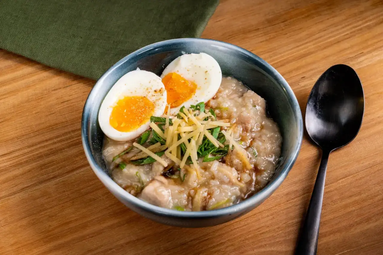 Herzhaftes Congee Rezept mit weichgekochtem Ei, Ingwer und Frühlingszwiebeln in einer Schüssel auf Holztisch.