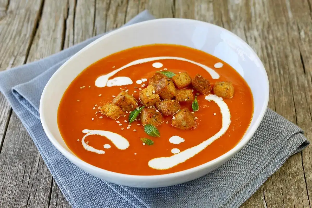 Eine Sch&uuml;ssel mit der besten Tomatensuppe, garniert mit Croutons, Minze und einem Klecks Sahne.