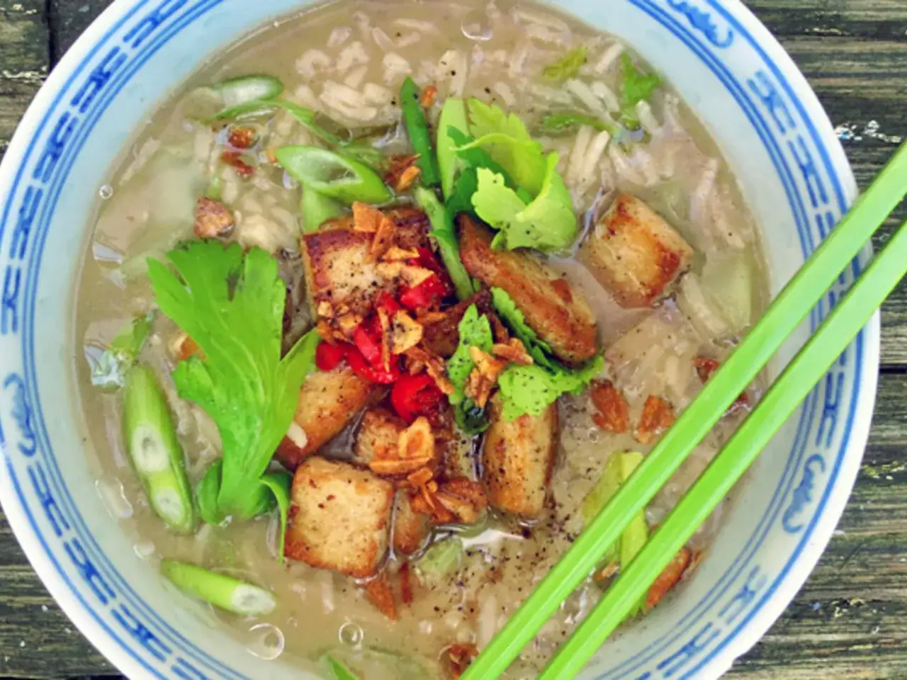 Khao tom: Eine Schüssel mit Reisbrei, garniert mit gebratenem Tofu, Frühlingszwiebeln und Kräutern.
