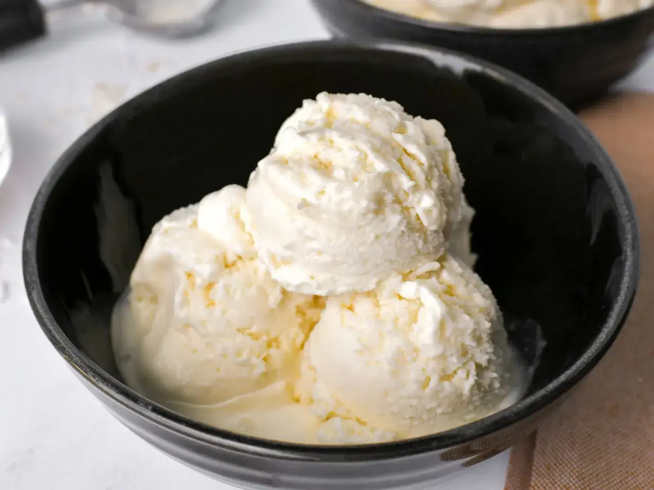 Cremiges Kokoseis selber machen: Drei Kugeln in einer schwarzen Schale, perfekt für heiße Tage.