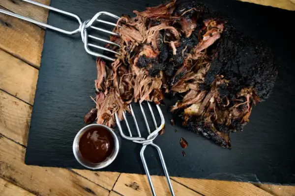 Saftiges pulled beef mit dunkler Kruste, serviert mit BBQ-Sauce.