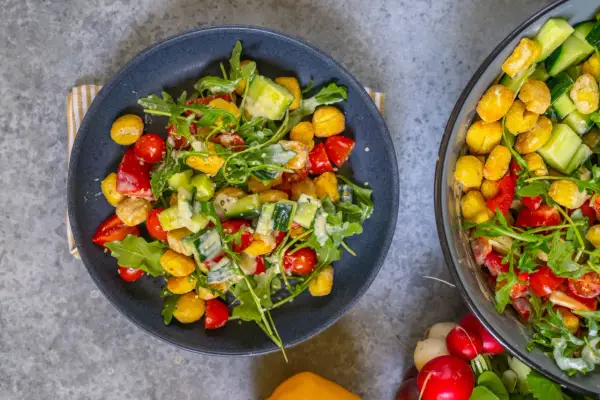 Knuspriger Gnocchi Salat aus dem Airfryer mit Tomaten, Gurken und Rucola, verfeinert mit einem cremigen Dressing.