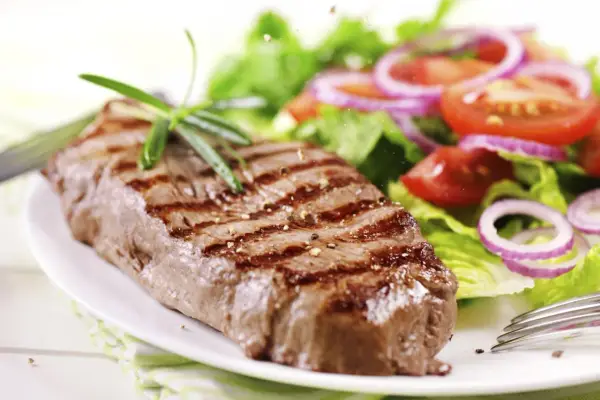 Ein saftiges Steak mit Grillstreifen, garniert mit Rosmarin, neben einem frischen Salat aus knackigem Grün, Tomaten und roten Zwiebelringen. Ein perfekter Steak Salat.