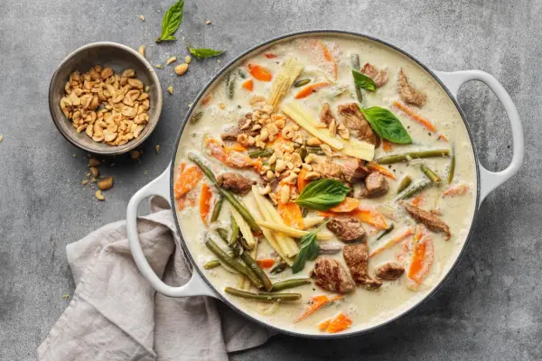 Herzhaftes Thai Curry mit Rindfleisch, zarten Möhren, grünen Bohnen und Maiskolben in cremiger Kokosmilch, garniert mit Erdnüssen und Basilikum.
