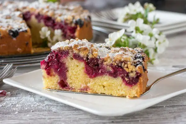 Ein saftiges Stück Streuselkuchen mit Marmelade und Puderzucker bestreut, bereit zum Genuss.