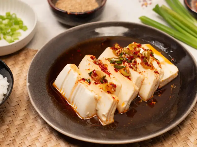 Seidiger Tofu, ein einfaches silken tofu recipe, serviert mit Frühlingszwiebeln und Chili-Öl auf einem dunklen Teller.