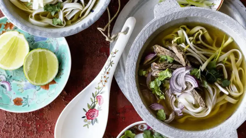 Ein dampfendes Pho-Rezept mit zarten Rindfleischscheiben, Reisnudeln, Sojasprossen und frischem Koriander in einer aromatischen Brühe. Dazu Limettenspalten.