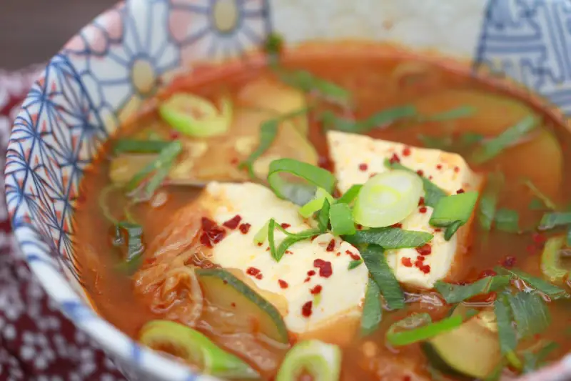 Heißes, würziges Sundubu Jjigae mit weichem Tofu, Kimchi und Frühlingszwiebeln in einer bunten Schüssel.