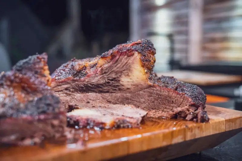 Saftiges Rind Brisket mit dunkler Kruste, auf einem Holzbrett serviert. Der Rauch steigt auf und verspricht ein zartes Geschmackserlebnis.